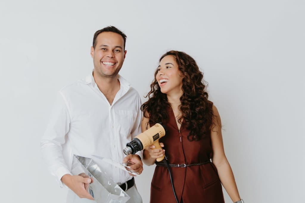 Eddie and Giselle, the couple who run Eddie Fixes LA, laughing with a heat gun and a drywall mud pan