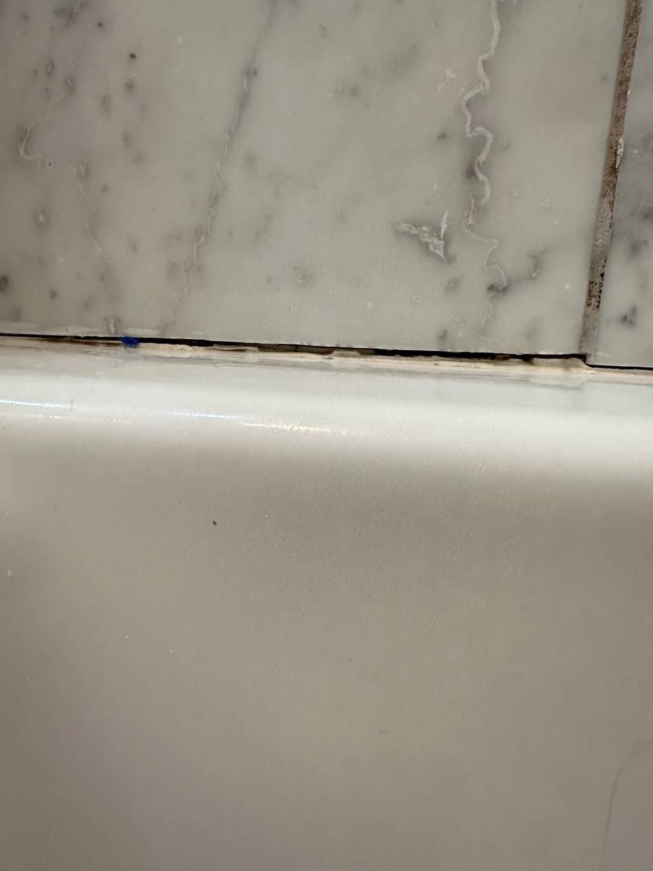 Cracked bathtub caulk corner with blue tape before resealing in West LA, CA 90025