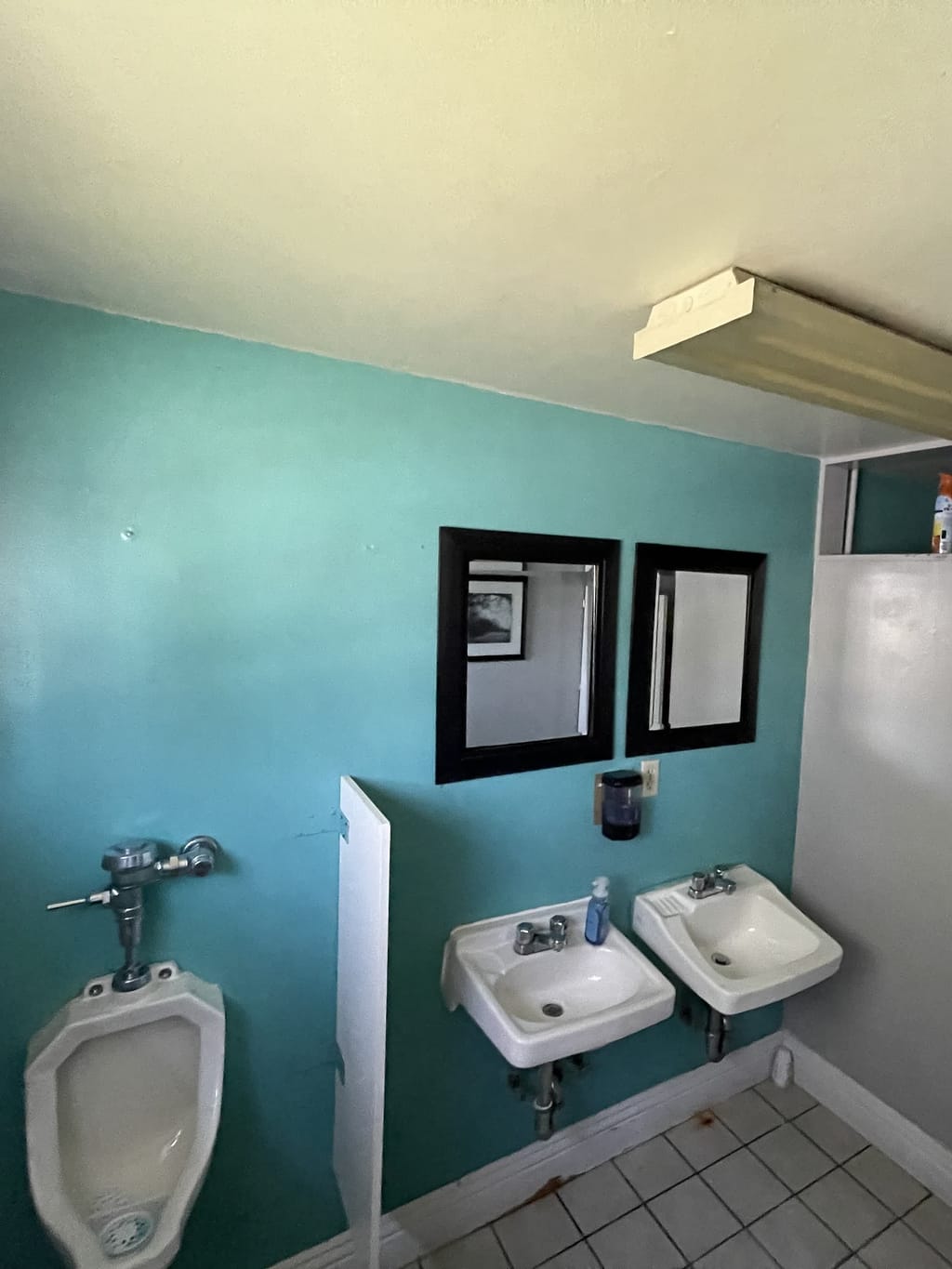 Church restroom with a rough teal wall, wall-hung sinks and urinal before repainting in Culver City, CA 90232