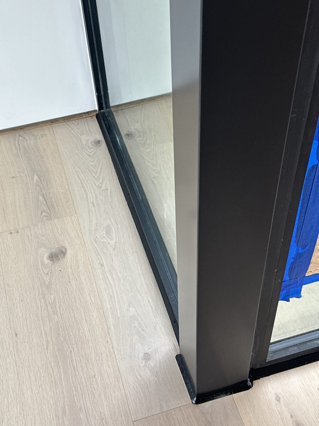 Blue tape masking the floor along a black glass partition before caulking in Malibu, CA 90265