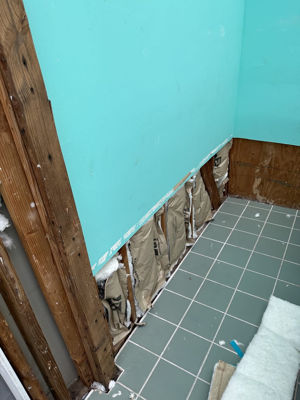 Lower wall opened up after water damage, exposing studs and insulation by a tiled floor in Glendale, CA 91207