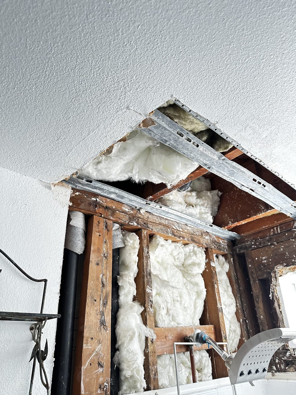 Open drywall hole above a shower exposing framing and insulation after a leak in North Hollywood, CA 91601