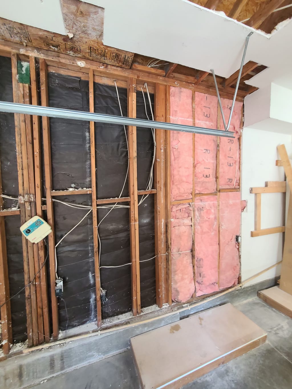 Garage wall stripped to studs with damaged insulation and open ceiling after a roof leak in Corona, CA 92882