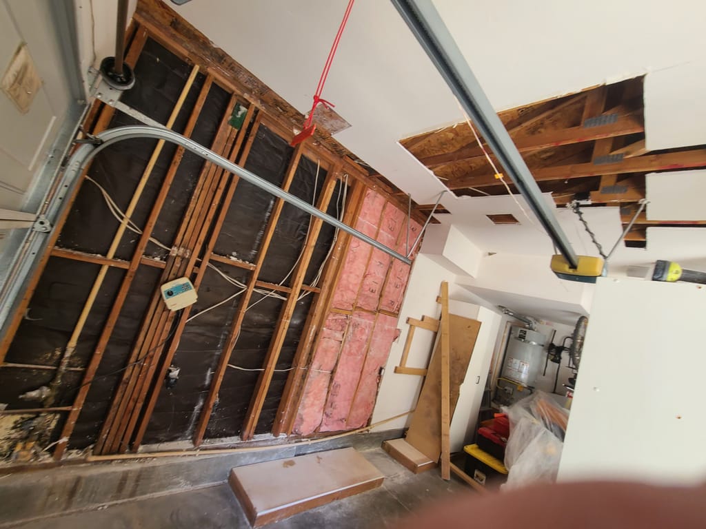 Wide view of a garage with drywall and insulation removed after water damage in Corona, CA 92882