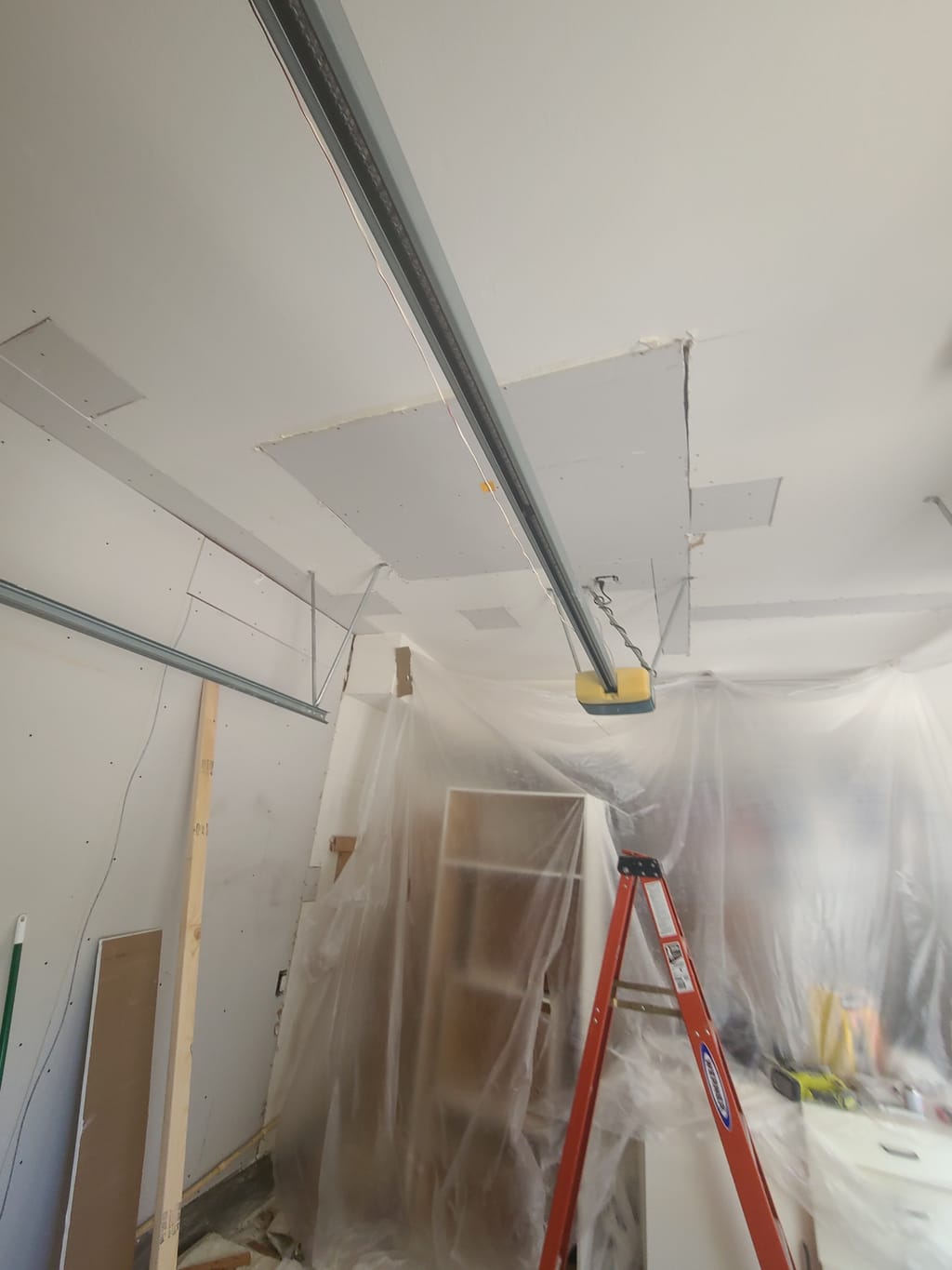 New drywall hung on the garage wall and ceiling with belongings protected in plastic in Corona, CA 92882