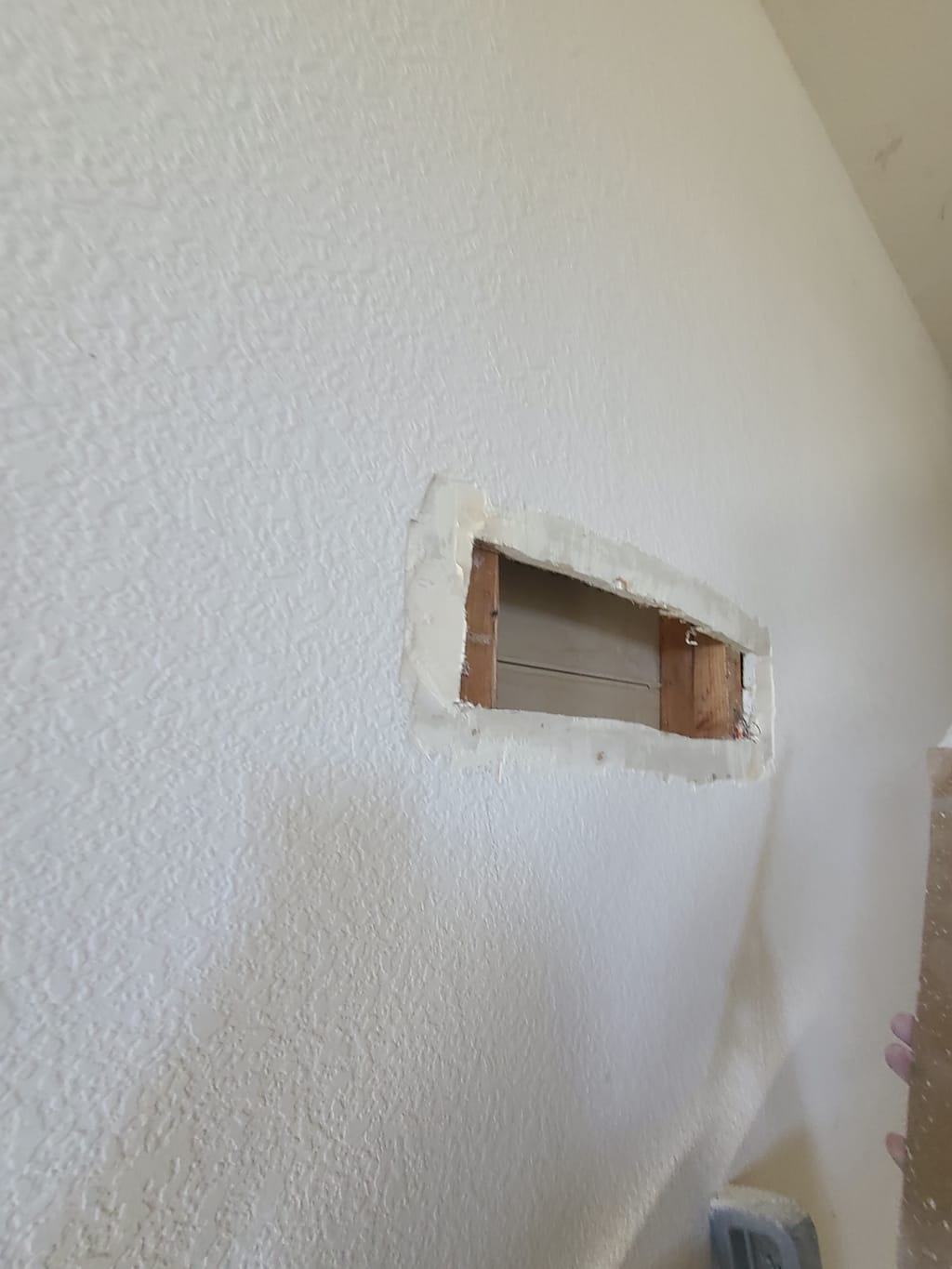Open drywall hole cut to the framing in a knockdown-textured wall in Corona, CA 92882